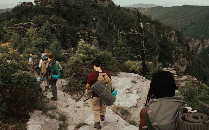 a group of teens wearing backpacks and hiking gear navigate a trail on a backpacking course with outward bound